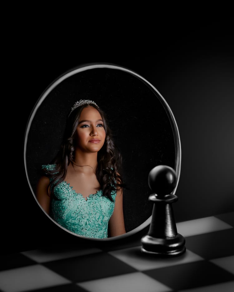 Una joven con vestido verde menta y tiara aparece reflejada en un espejo circular, sobre un piso de tablero de ajedrez. En primer plano, un peón negro.