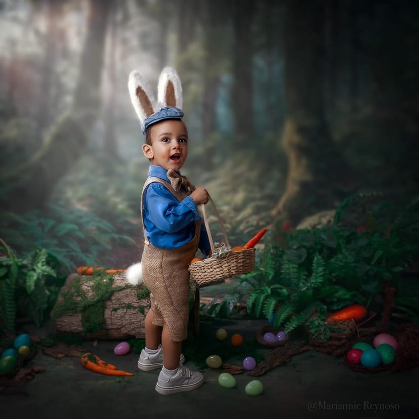 Niño pequeño con orejas de conejo, gorra y tirantes, cargando una cesta de mimbre con zanahorias. A su alrededor, huevos de Pascua de colores sobre un fondo pictórico de bosque.
